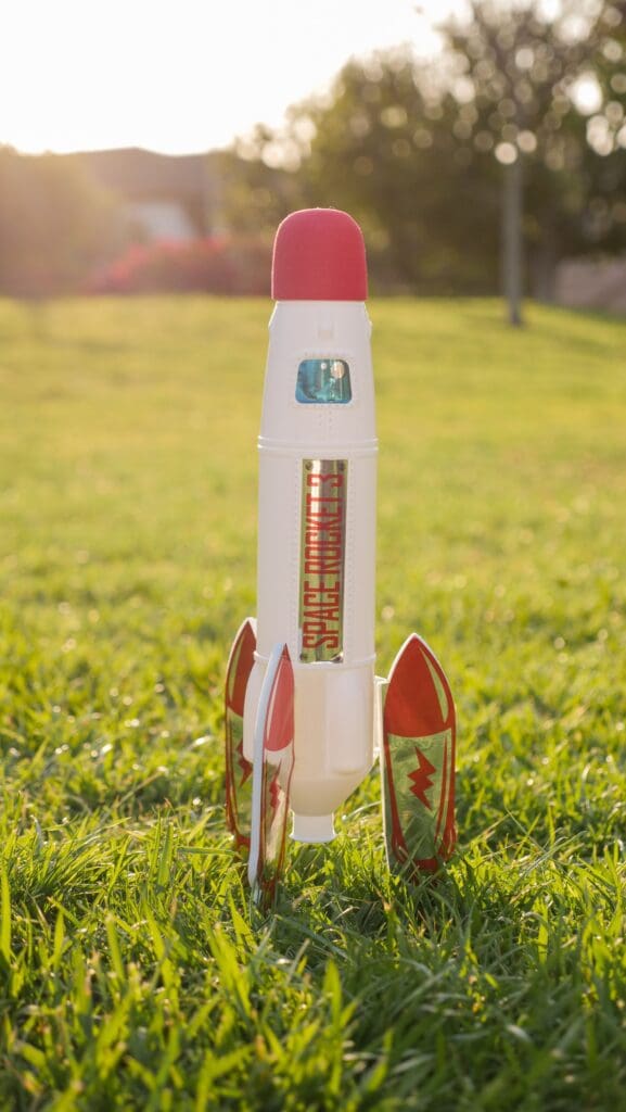 Toy space rocket standing in grass at sunset