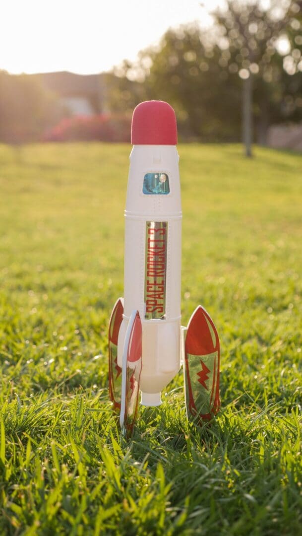 Toy space rocket standing in grass at sunset